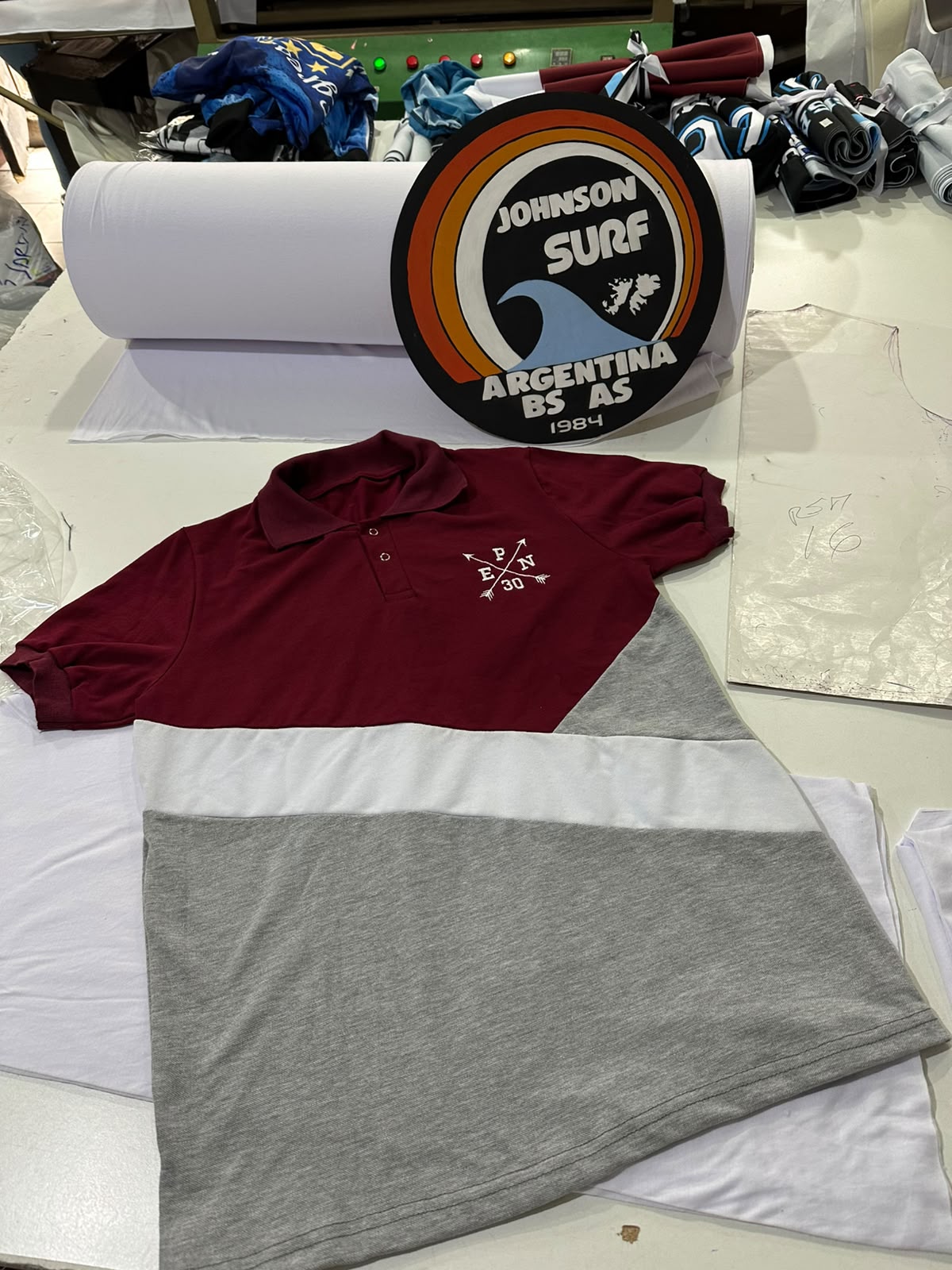 Remera bordó y buzo gris con escudo estampado, sobre una mesa clara