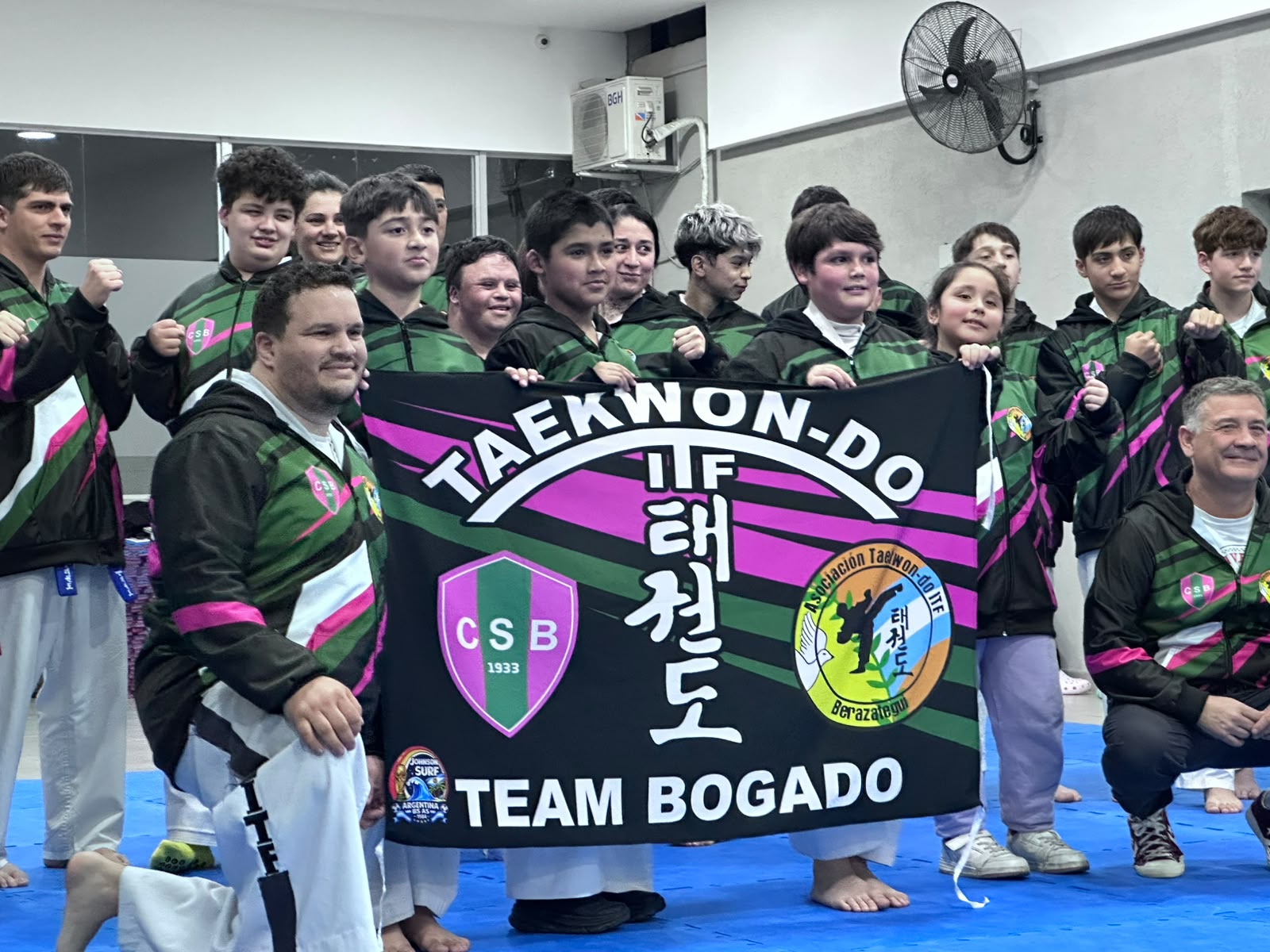Equipo de taekwondo posando con camperas estampadas y una bandera del club